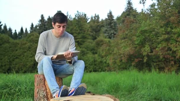 Genç adam bir parkta oturan ve bir kitap okuma — Stok video