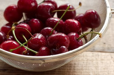 Kirazlar ahşap masada, su damlaları makro arka planda.