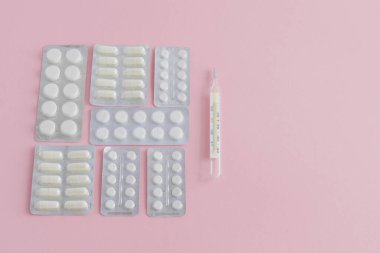 Vücut ısısını ölçmek için civa termometresi pembe arka planda tedavi için kabarcıklarda haplar ve kapsüller bulunan bir set.