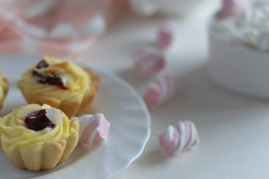Beyaz çay tabağında bademli meyveli kek, porselen bardakta mini marşmelov. Arka planda yakın plan fotoğrafı. Seçici odak. 