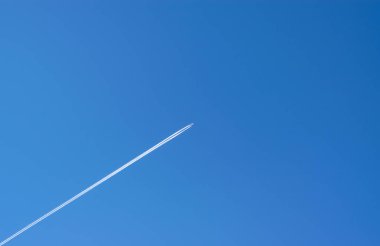Seyahat, tatil konsepti. Yüksekten uçan bir uçak, mavi gökyüzüne karşı beyaz bir iz bırakıyor. Mesajın için yer aç. Yatay fotoğraf.