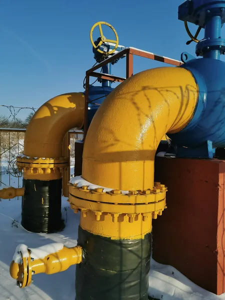 Parlak mavi bir gökyüzünün arka planında, sarı-mavi boruları olan bir gaz kompresör istasyonu. Gaz endüstrisi. Dikey fotoğraf. 