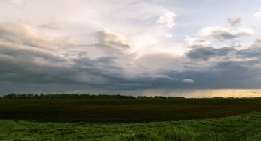 Kırsal kesimdeki tarıma elverişli bir arazide gök gürültülü bulutlar. Akşam vakti. Bir çiftlik, tarlaya sürülmüş bir tarla. Yatay fotoğraf. 