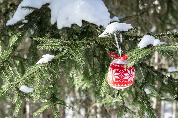 Christmas concept, postcard, wallpaper. On the spruce branches with white snow hangs a red Christmas tree decoration with an ornament. Horizontal photo.