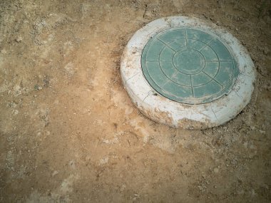 Bir toprak parçasında kanalizasyon kapağı. Kanalizasyon iyi. Merkez caddedeki su ve kanalizasyon şebekeleriyle bağlantılı. Yatay fotoğraf.