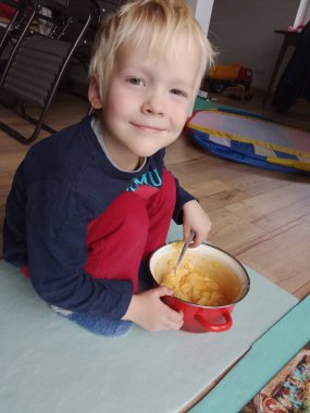 Çocuk, annesinin yemek hazırlamasına yardım etmekten mutluluk duyar. Hamuru kaşıkla yoğurur.