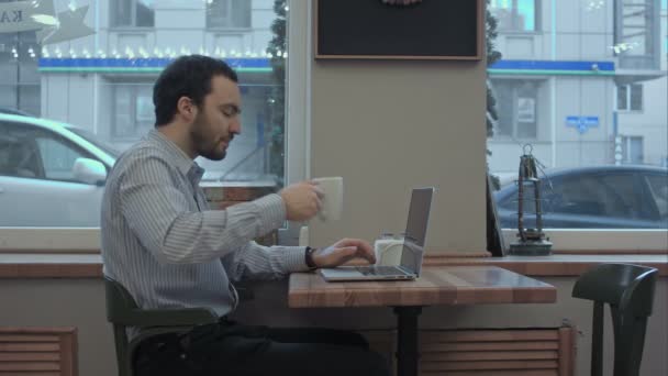 Joven empresario exitoso está trabajando en su computadora portátil en la cafetería y beber café — Vídeo de stock