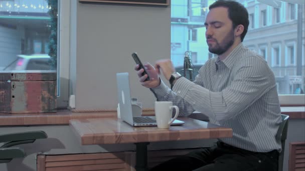 Ernstige zakenman met behulp van mobiele telefoon tijdens de koffiepauze in café, zijn horloge kijken — Stockvideo