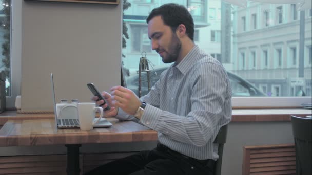 Úspěšný mladý podnikatel pomocí mobilní telefon během přestávky na kávu v kavárně uvnitř — Stock video