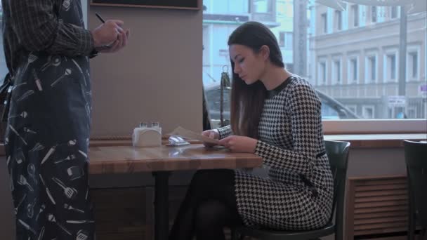 Mooi meisje maakt een order. De ober luistert aandachtig naar haar en schrijf alles op wat — Stockvideo