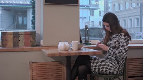 Chica mensajes de texto en el teléfono inteligente en un café — Vídeo de stock