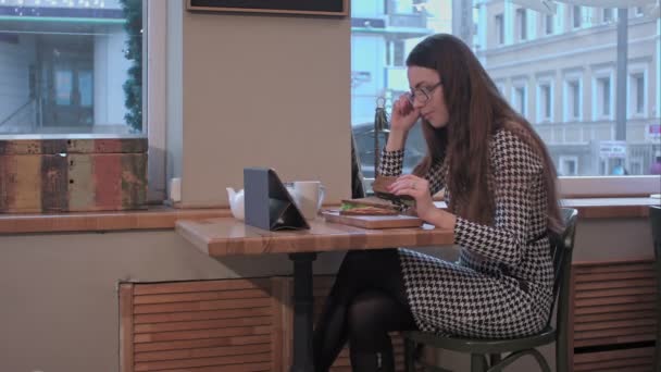 Business κυρία χρησιμοποιώντας tablet ενώ τρώει σάντουιτς στο καφενείο — Αρχείο Βίντεο