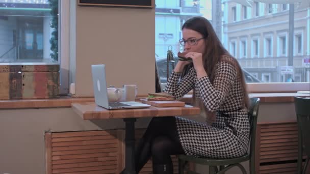 Jonge vrouw gebruik laptop terwijl eet broodje in het café tijdens de businesslunch — Stockvideo