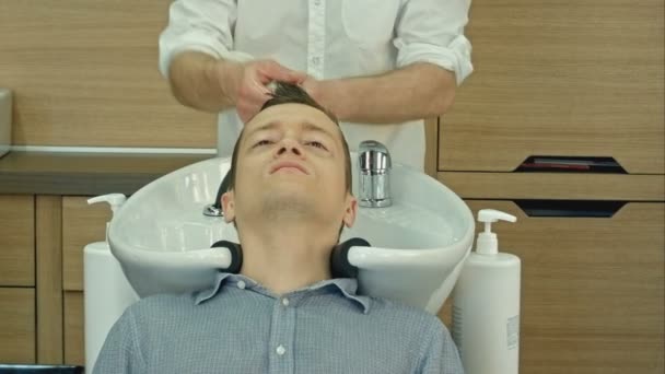 Красивий чоловік миє волосся в перукарні. Молодий чоловік лежить з закритими очима в салоні краси . — стокове відео