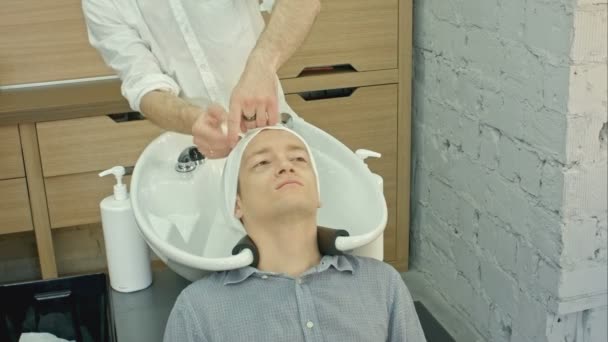 Fryzjer fryzjerka mycie włosów klienta - młody człowiek wypoczywa w Beauty salon fryzjerski — Wideo stockowe