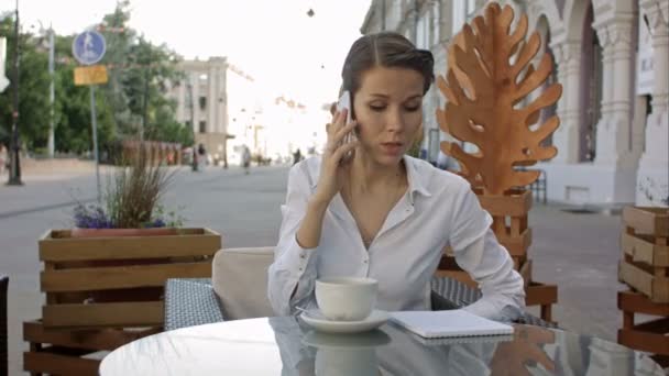 年轻的商业妇女的肖像坐在户外咖啡馆放松喝咖啡, 打电话给她的手机 — 图库视频影像