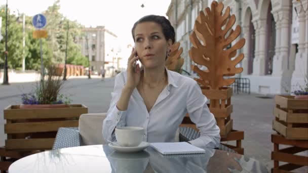 Kafede kahve içip cep telefonuyla konuşan genç bir kadın. — Stok video