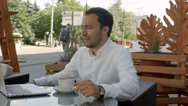 Trabajar y relajarse. Conferencia en línea. Empresario vestido con camisa de trabajo con portátil, hablando por Skype en la cafetería del parque al aire libre — Vídeos de Stock