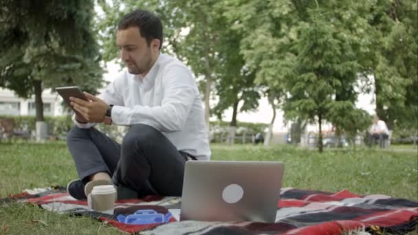 Tablet, laptop, cep telefonu parkta kullanarak genç başarı işadamı — Stok video