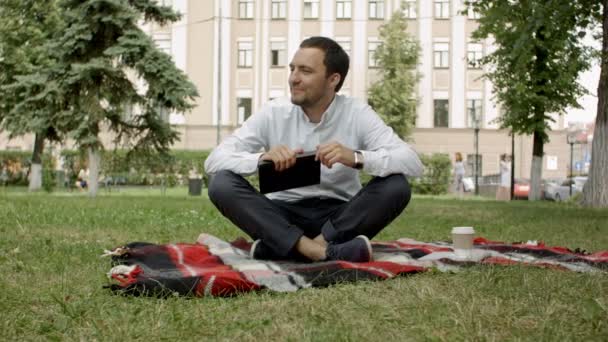 Junger Mann ruht sich in einem Park mit einem Buch und Coffee to go aus — Stockvideo