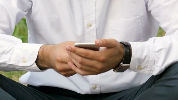Ο άνθρωπος, πληκτρολογώντας το μήνυμα στο smart phone στο πάρκο. Εστίαση στα χέρια. — Αρχείο Βίντεο