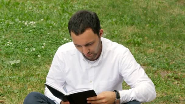Entspannter junger Mann liest Buch in der Natur — Stockvideo