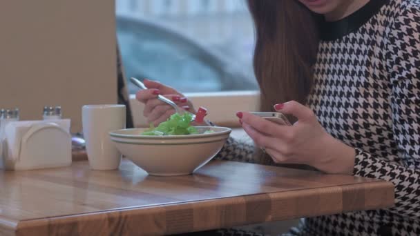 Braços de jovem empresária usando um smartphone para comunicação. Ela está sentada à mesa no café e comendo uma salada — Vídeo de Stock