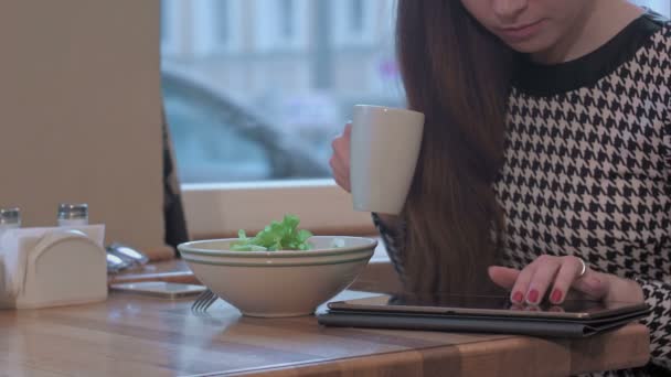 Brazos de joven empresaria utilizando una tableta para la comunicación. Ella está sentada en la mesa en el café y comiendo una ensalada — Vídeos de Stock