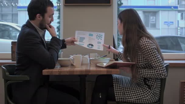 Επιχειρηματικός άνθρωπος εξηγήσει το διάγραμμα στο βοηθό στο μεσημεριανό γεύμα στο καφέ — Αρχείο Βίντεο