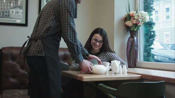 カフェで女性にお茶のやかんを与える男ウェイター. — ストック動画