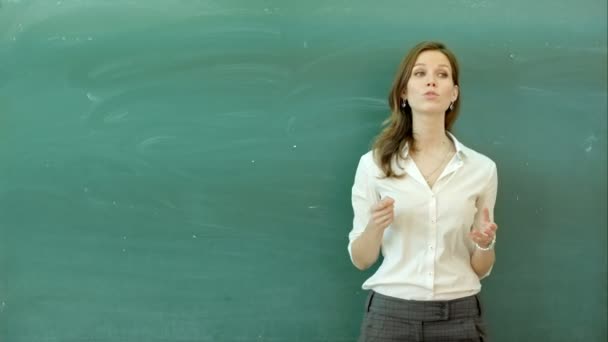 Happy teacher standing in front of black board, talking on camera — Stock Video