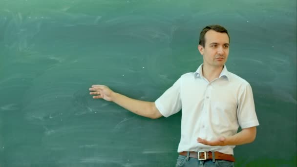 Young male teacher pointing at blank blackboard and talking — Stock Video