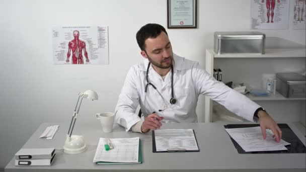Mladý lékař vážné ničí sedí v ordinaci se složkou Dokumenty — Stock video