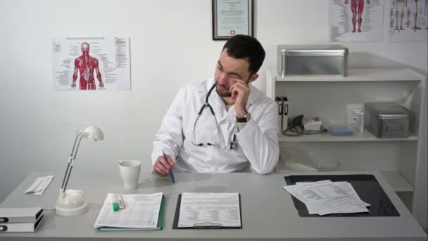 Médico barbudo serio sentado en el consultorio médico y pensando en el tratamiento — Vídeos de Stock