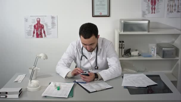 Medico utilizzando il suo smartphone in ufficio alla scrivania — Video Stock