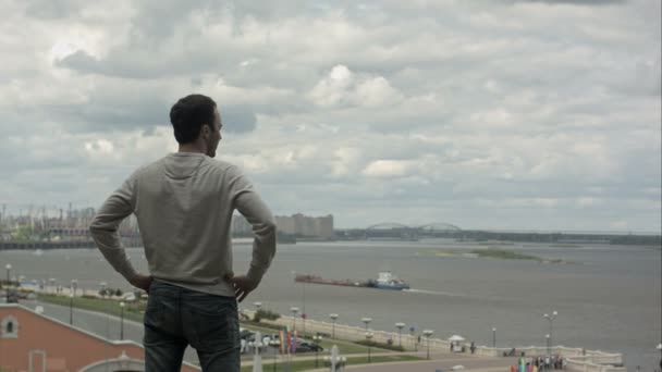 Jovem bonito de pé perto do rio e olhando para a frente . — Vídeo de Stock