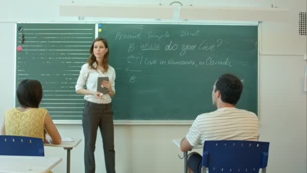 Jonge vrouwelijke leraar schrijven op schoolbord in de klas — Stockvideo