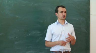 Blackboard yakınındaki bir şey söyleyeyim genç öğretmen ve öğrenci gesticulate.