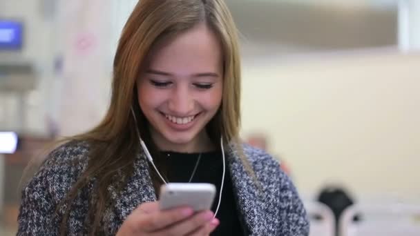 Pasajera en la estación aérea escuchando algo en un smartphone. Las niñas sonríen y usan la pantalla táctil de su gadget — Vídeo de stock