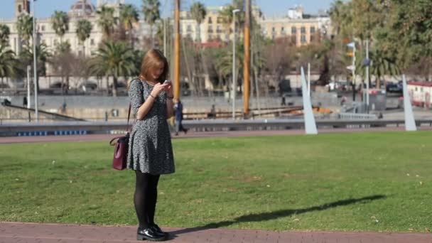 Девушка в платье на фоне реки со смартфоном — стоковое видео