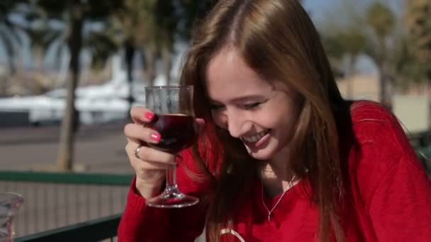 Beautiful young girl with glass of red wine alone in a street cafe. — Stock Video