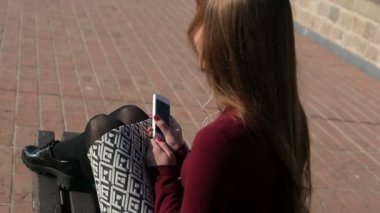 esmer elbise içinde bankta oturur ve kulaklık ve cep telefonu ile müzik dinlerken, üst görünümü