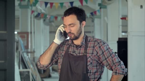 Jonge werknemers in werkplaats praten aan de telefoon met baard. — Stockvideo