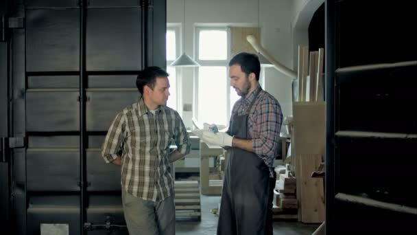 Twee schrijnwerkers in de fabriek bespreken in ongeveer iets. — Stockvideo