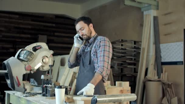 Carpenter working on his craft in a dusty workshop and speak phone. — Stock Video