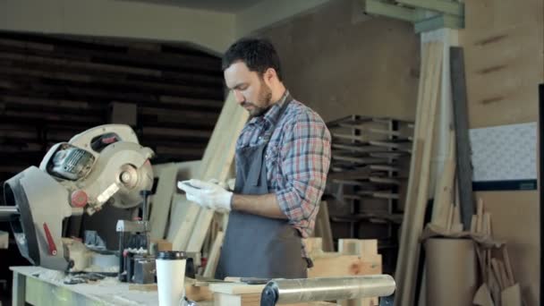 Плотник с бородой делает что-то на своем смартфоне в мастерской . — стоковое видео