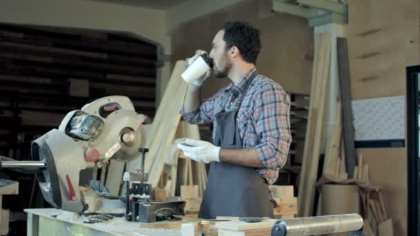 Falegname in piedi vicino sega elettrica nel suo laboratorio e bere caffè . — Video Stock