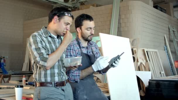 Dos carpinteros discutiendo el trabajo y uno de ellos comiendo en el taller . — Vídeos de Stock