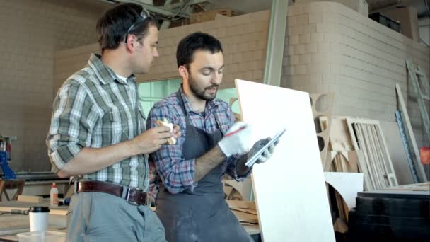 Two carpenters discussing work one of them eating and another is writing in notebook at workshop. — Stock Video