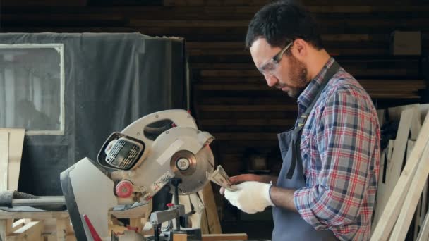 Bearded carpenter count money in workshop near electric saw. — Stock Video